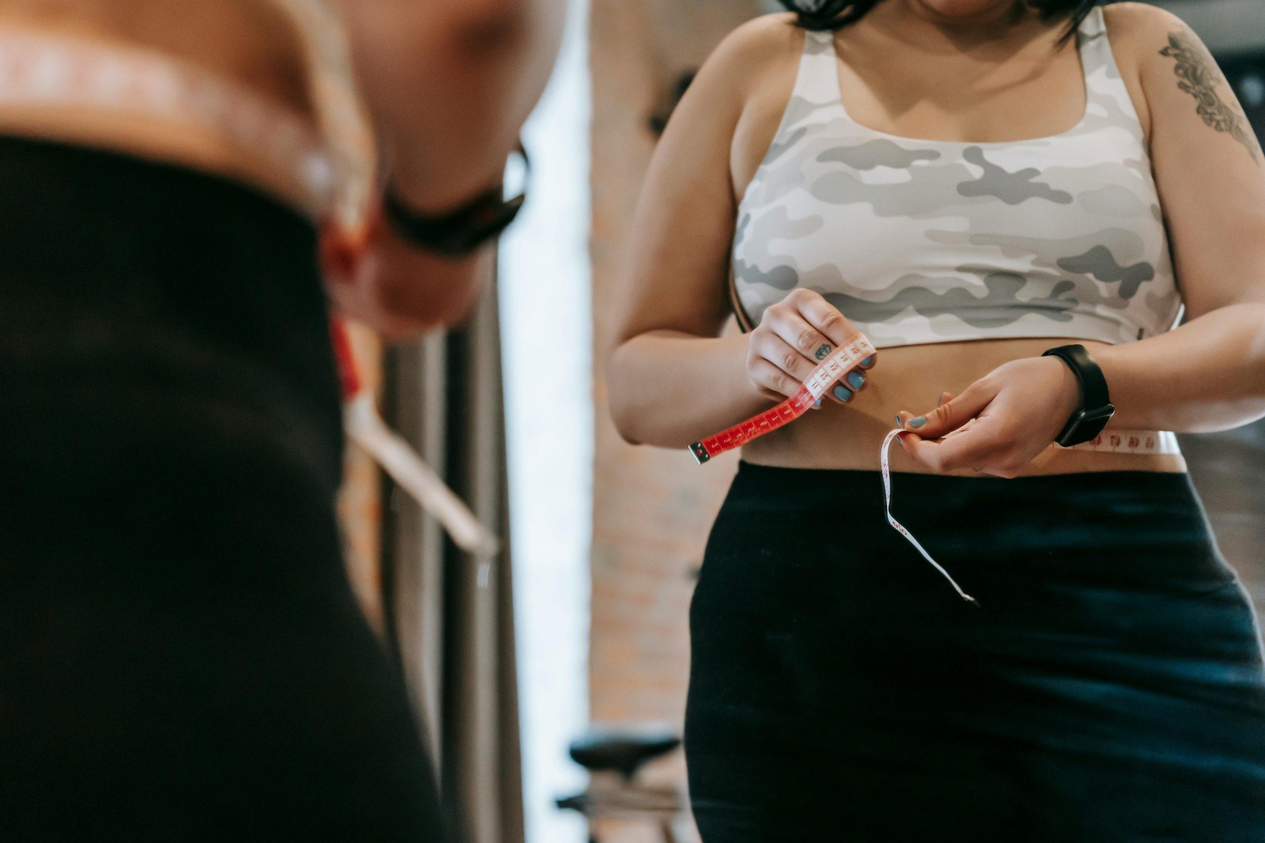 Woman measuring waist in the mirror for weight loss