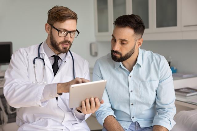 Male physician discussing testosterone therapy and fertility planning with middle-aged male patient in Woodbury clinic